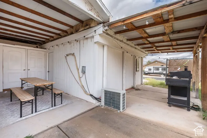 Covered outdoor patio area featuring a concrete slab, wood-beam ceiling structure, and dual-door entry access