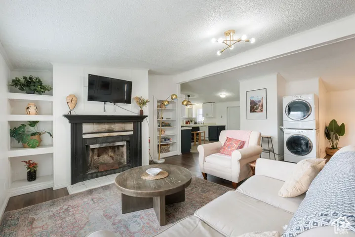 Fireplace with a black mantel, built-in shelving, wood-finish flooring, and stacked laundry unit