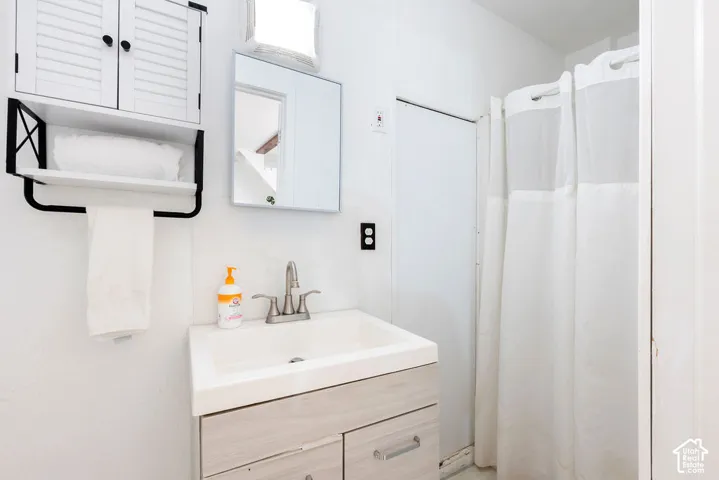 Bathroom featuring a vanity with wood-finish cabinetry, integrated rectangular sink, wall-mounted cabinet with louvered doors, square mirror, and a tub-shower combination