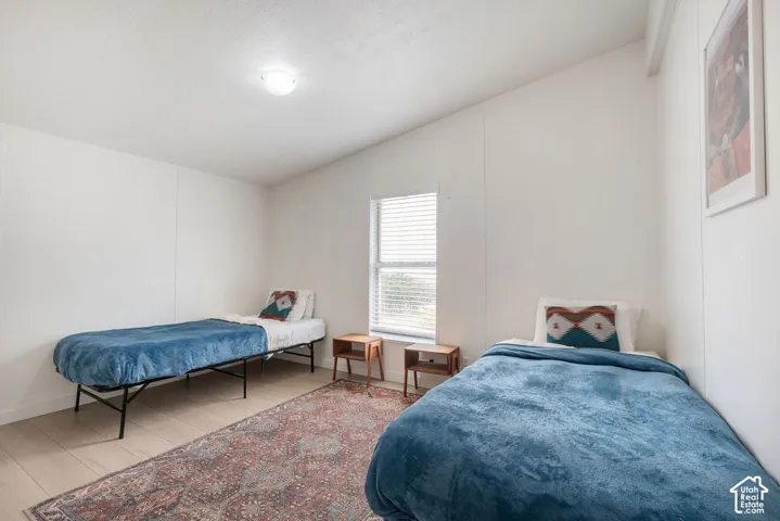 Neutral-toned walls, wood-finish flooring, vaulted ceiling, and a central window with horizontal blinds