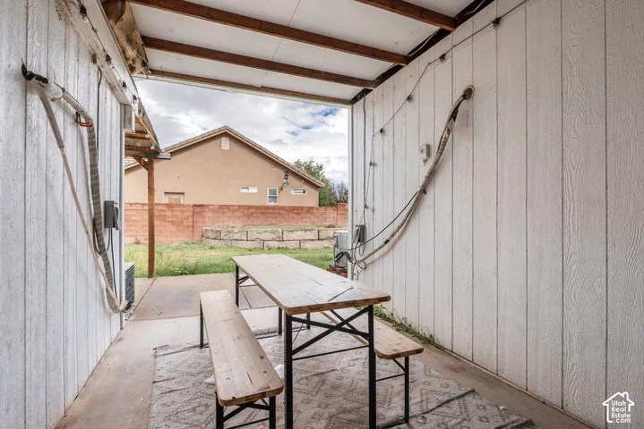 Covered outdoor patio featuring vertical wood-plank siding, exposed rafter beams, and a concrete floor