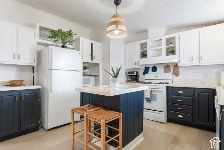 Kitchen featuring a two-tone cabinetry scheme, center island with stone-finish countertop, white appliances, and wood-finish flooring