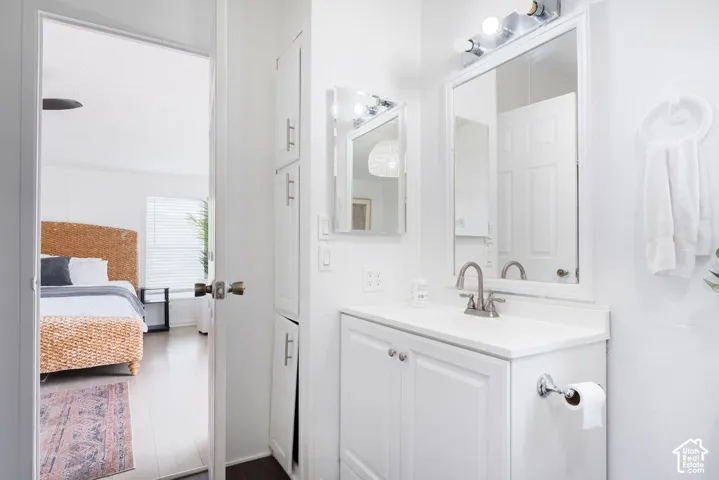 Bathroom featuring a white vanity with an integrated countertop, chrome faucet, tall built-in storage cabinetry, and a framed wall mirror with a multi-bulb light fixture