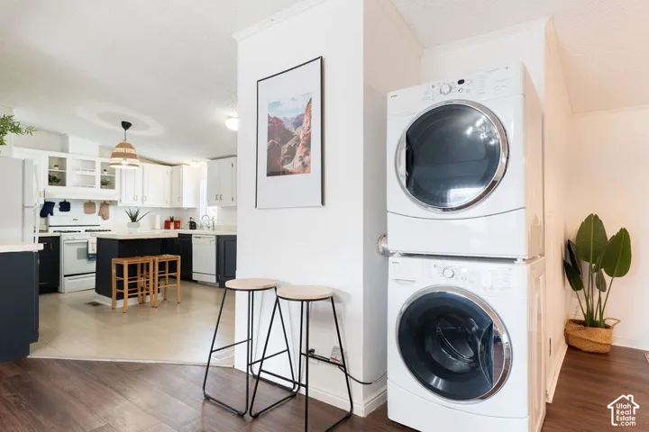 Laundry area featuring a stackable washer and dryer unit, wood-finish flooring, and white cabinetry