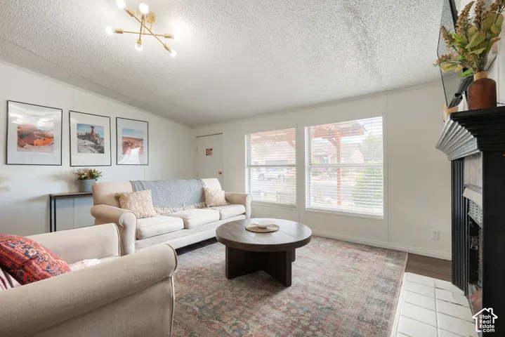 Living area featuring a fireplace with a black mantel and tile surround, dual windows with horizontal blinds, and a gold-tone multi-arm overhead light fixture