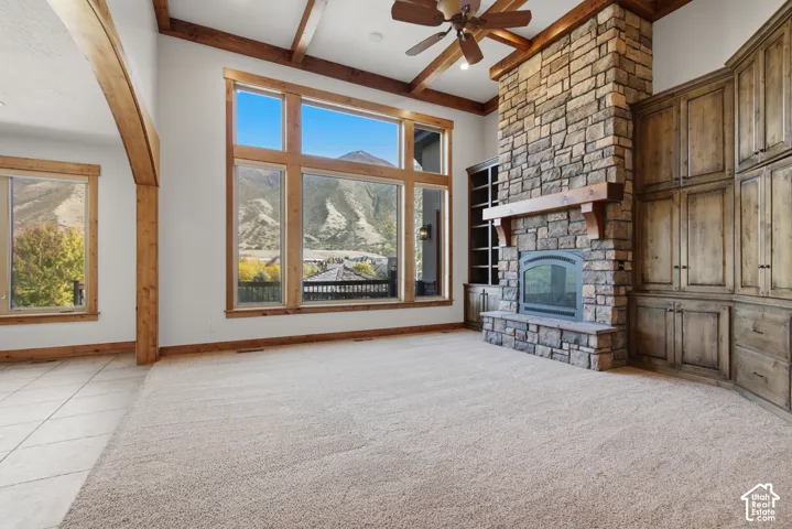 Living area featuring a floor-to-ceiling stone fireplace with a wood mantel, built-in wooden cabinetry, vaulted ceilings with exposed wood beams, large windows with mountain scenery, and a ceiling fan