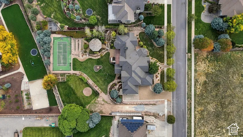 Aerial view featuring a multi-gabled roofline, private tennis court, detached gazebo, expansive lawn, and mature landscaping