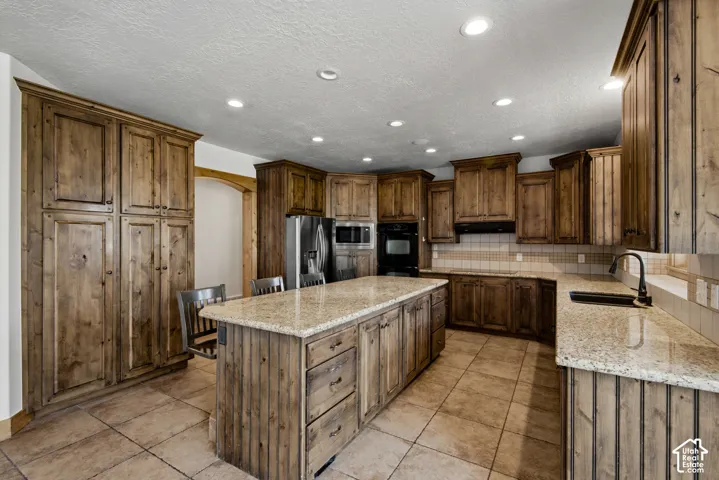 Kitchen featuring stained wood cabinetry, stone countertops, central island, tiled flooring, and recessed ceiling lighting