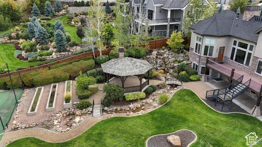 Landscaped backyard featuring a covered gazebo, multi-level rock waterfall, dedicated tennis court, and terraced stone planting beds