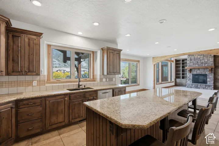 Kitchen featuring wood cabinetry, stone-surface countertops, central island, tile flooring, and a stone-faced fireplace