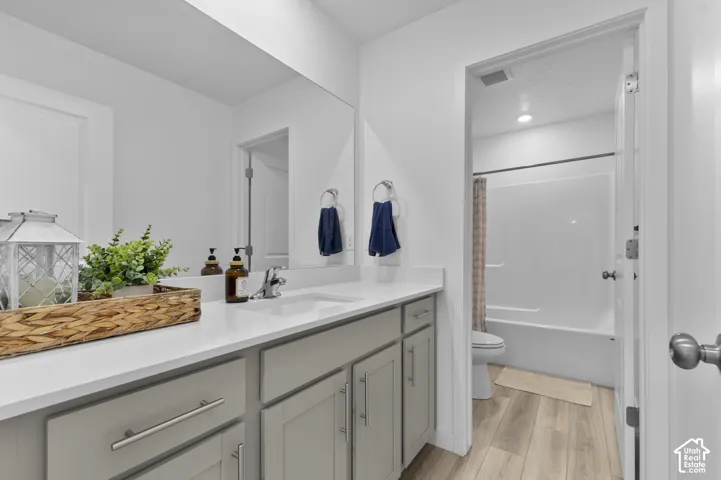 Grey cabinetry vanity with white countertop, integrated rectangular sink, full-width mirror, and wood-finish flooring