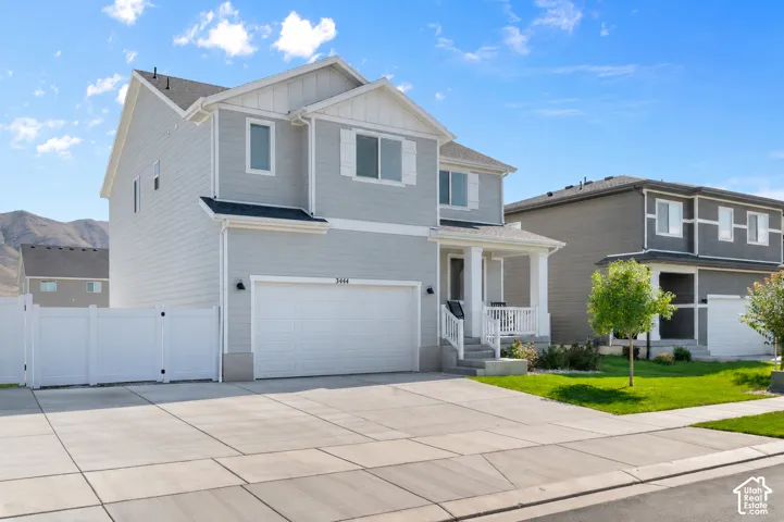 Two-story residence featuring light gray horizontal siding, a covered front porch with white railing, an attached two-car garage, and a white vinyl privacy fence