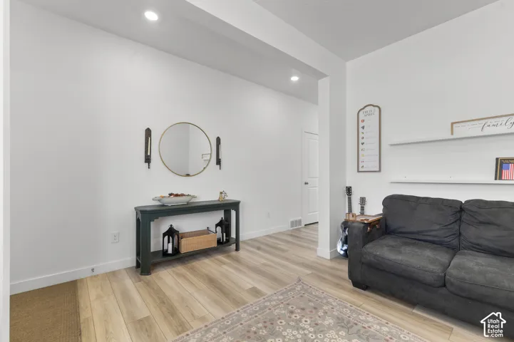 Neutral-toned wood-finish flooring, recessed lighting, and wall-mounted white floating shelves