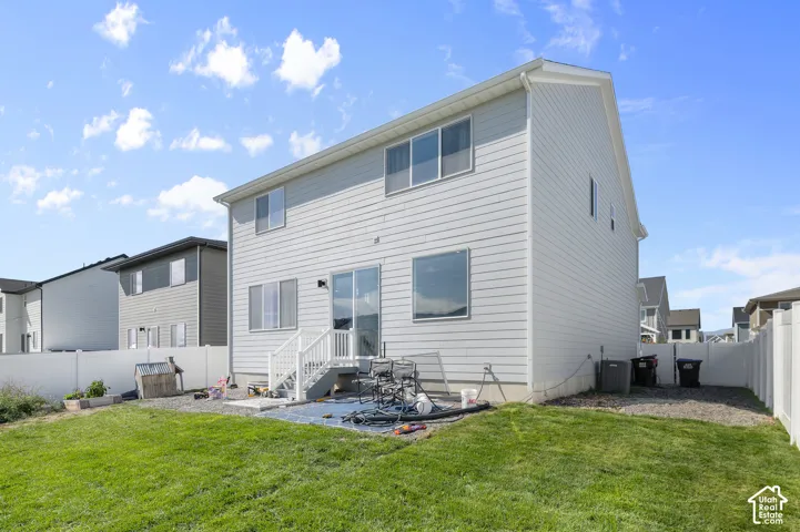 Two-story residence featuring light gray horizontal siding, a concrete patio, white vinyl privacy fencing, and a built-in staircase with white railings