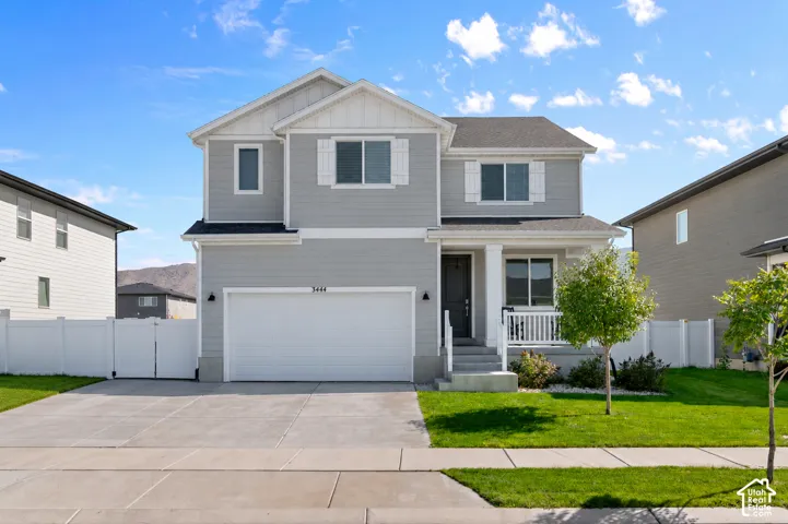 Two-story residence featuring horizontal siding, a covered front porch with white railing, a double-car garage, and perimeter white vinyl fencing