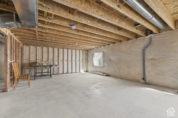 Unfinished lower level featuring exposed wood-joist ceiling, concrete flooring, exterior window, and vapor-barrier wall insulation