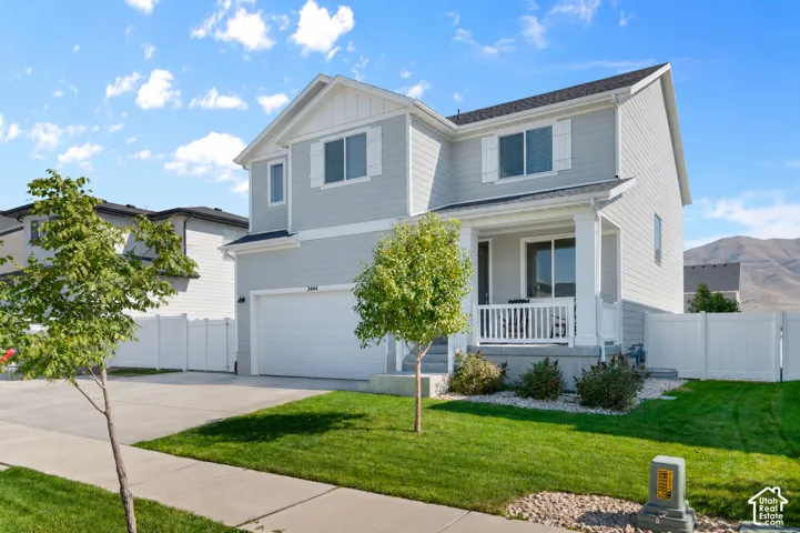 Two-story exterior featuring light gray horizontal siding, a covered front porch with white railing, a concrete driveway, and an attached two-car garage
