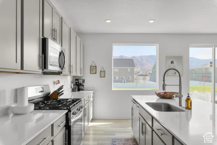 Kitchen featuring light gray cabinetry, quartz countertops, a stainless steel gas range with built-in microwave, a center island with undermount sink and high-arc faucet, and recessed lighting