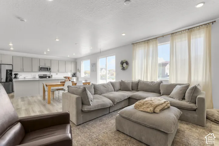 Open-concept living space featuring wood-finish flooring, recessed lighting, neutral-toned cabinetry, a peninsula countertop, and large windows with integrated hardware