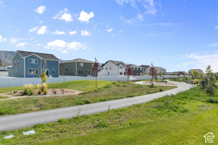 Asphalt paved pathway extending through a grass-covered common area with landscaped mounds, ornamental plantings, and white vinyl privacy fencing