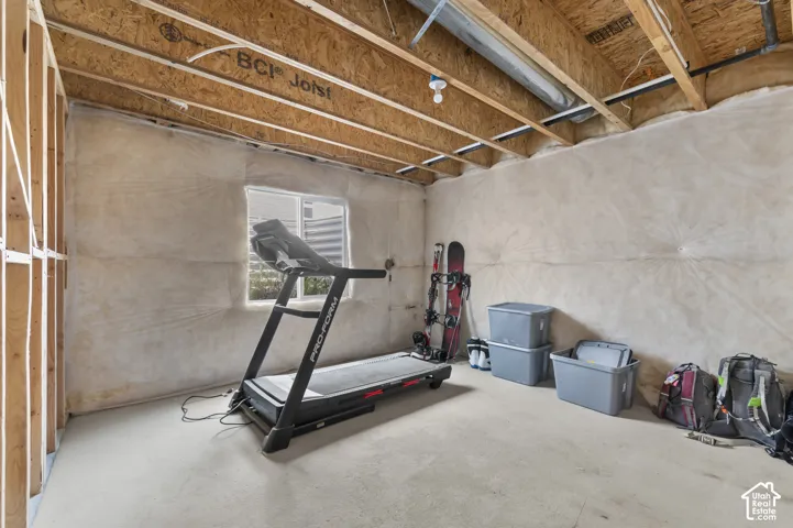 Unfinished space featuring exposed engineered wood joists, concrete flooring, and insulated walls with a single slider window
