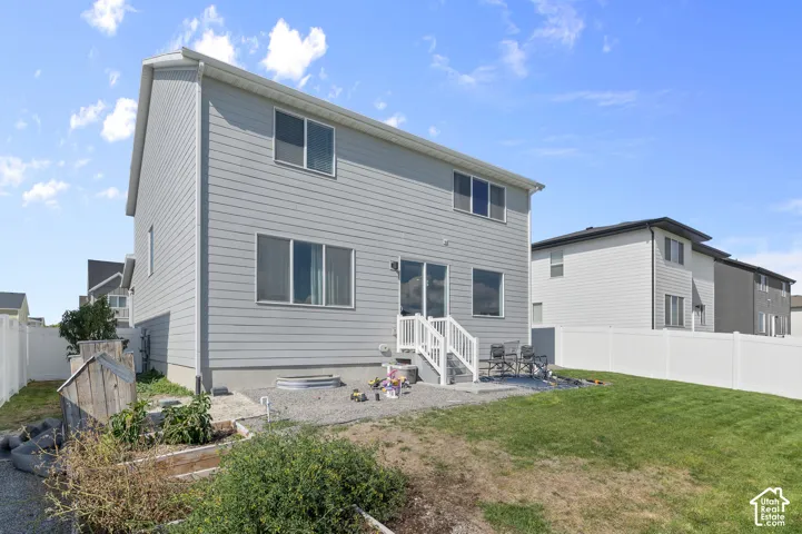 Two-story exterior featuring horizontal light-toned siding, white vinyl fencing, a gravel patio area, raised garden beds, and an elevated entryway with white railings