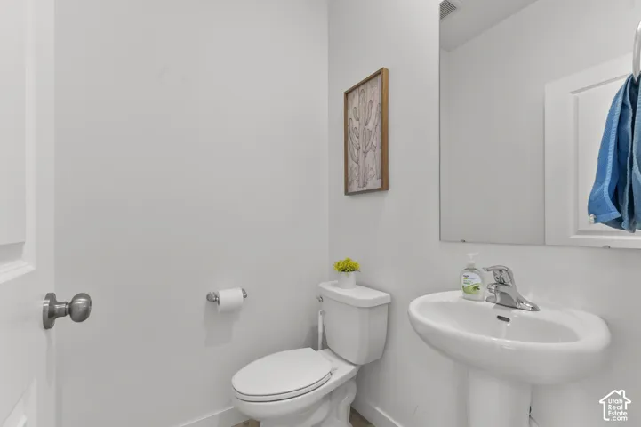 White pedestal sink with chrome faucet, large wall-mounted mirror, and standard porcelain toilet