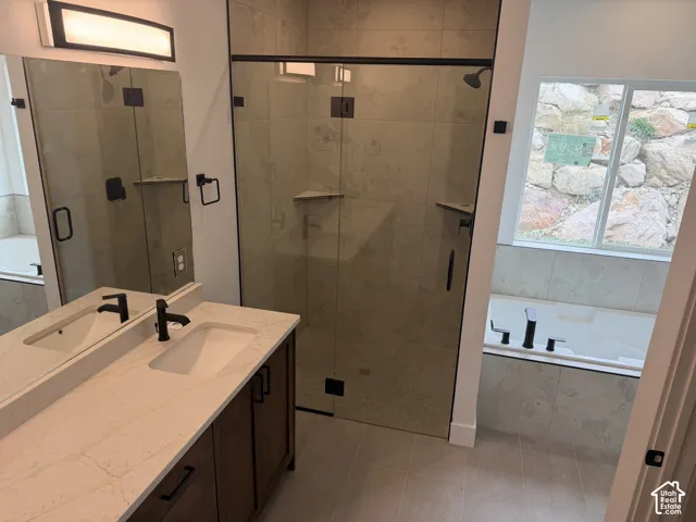Bathroom featuring a stone-topped vanity with matte black fixtures, a walk-in glass-enclosed shower with tile surround, a built-in soaking tub, and large-format floor tiling