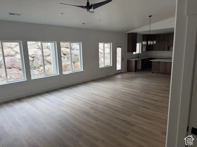 Open-concept interior featuring wood-finish flooring, vaulted ceilings, expansive sliding windows, and dark-toned cabinetry with light-colored countertops
