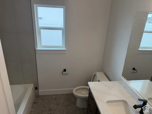 Bathroom featuring a white composite vanity with quartz countertop, undermount sink, matte black hardware, textured floor tiling, and a tub with a grey tile surround