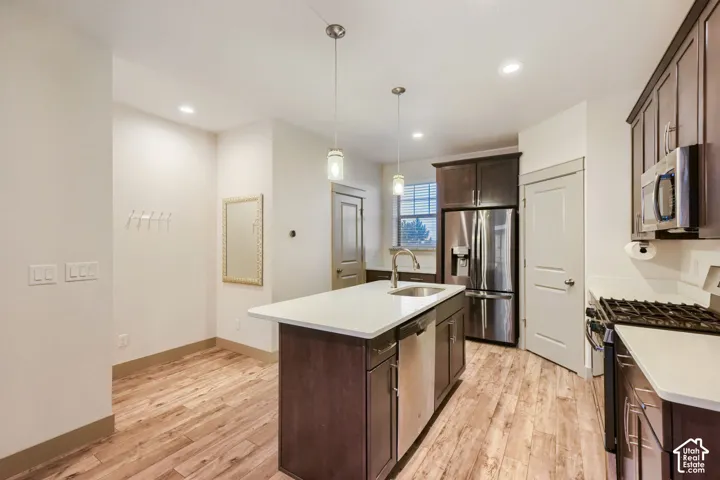 Kitchen featuring dark-finish cabinetry, stone-surface countertops, wood-finish flooring, a stainless steel appliance suite, and dual pendant lighting
