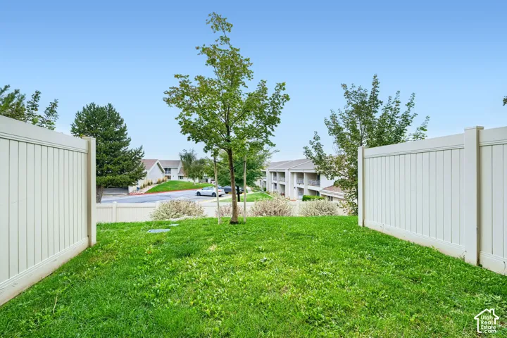 Private backyard featuring a grass lawn, perimeter vinyl fencing, and mature trees