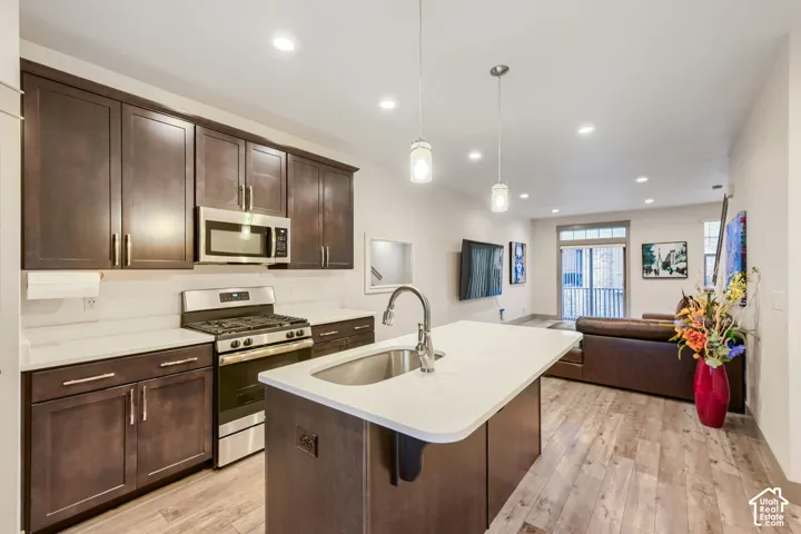 Kitchen featuring dark-toned cabinetry, quartz countertops, a central island with an undermount sink, stainless steel appliances, and wood-finish flooring
