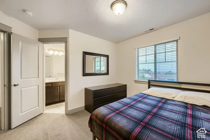 Neutral interior space with wall-to-wall carpeting, window with slatted blinds, and attached bathroom featuring dark-toned cabinetry
