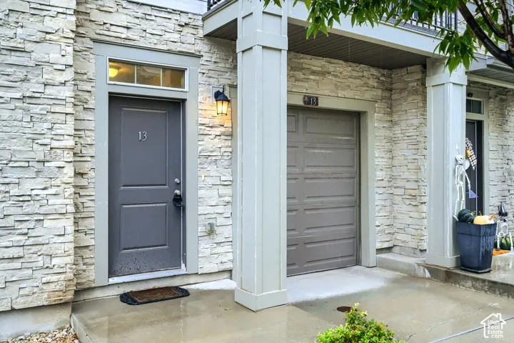 Exterior facade featuring stacked stone masonry, a paneled entry door with a transom window, a single-car garage, and columned architectural detailing