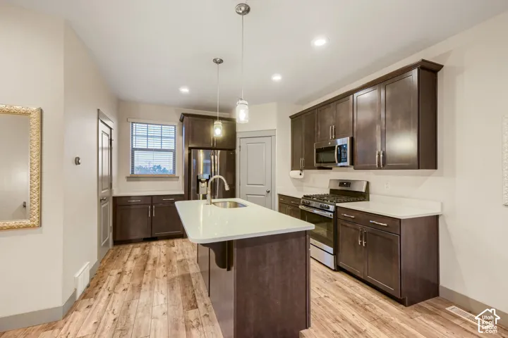 Kitchen featuring dark-finish cabinetry, stone-surface countertops, stainless steel appliances, a center island with an integrated sink, and wood-finish flooring