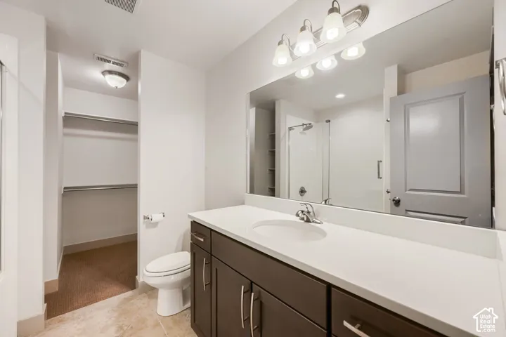 Bathroom featuring a dark wood-finish vanity with a stone countertop, an oval undermount sink, a full-width wall mirror, and integrated walk-in closet shelving