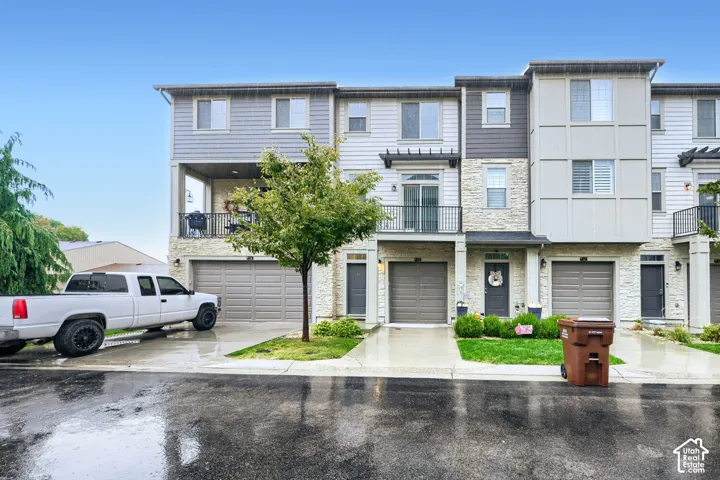 Multi-story townhome exterior featuring stone masonry cladding, horizontal siding, attached garages, and private balconies with metal railings