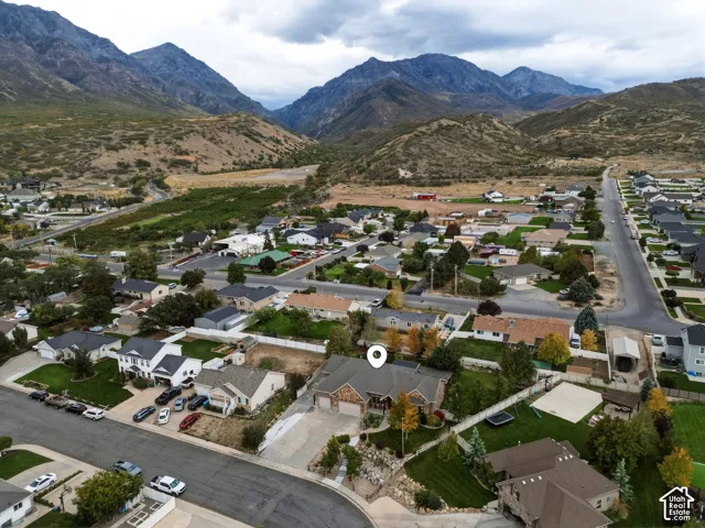 Aerial perspective of a multi-gabled residence featuring a multi-car garage, stone facade accents, concrete driveway, and expansive mountain terrain background