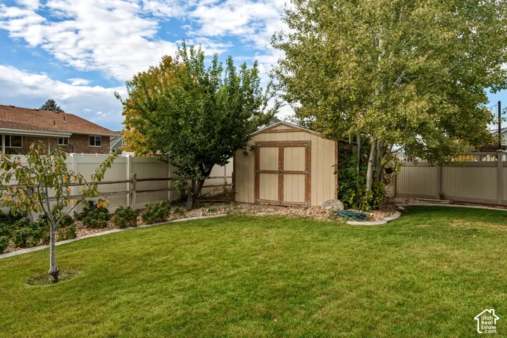 Backyard featuring a detached storage shed, privacy fencing, stone ground cover, and mature trees