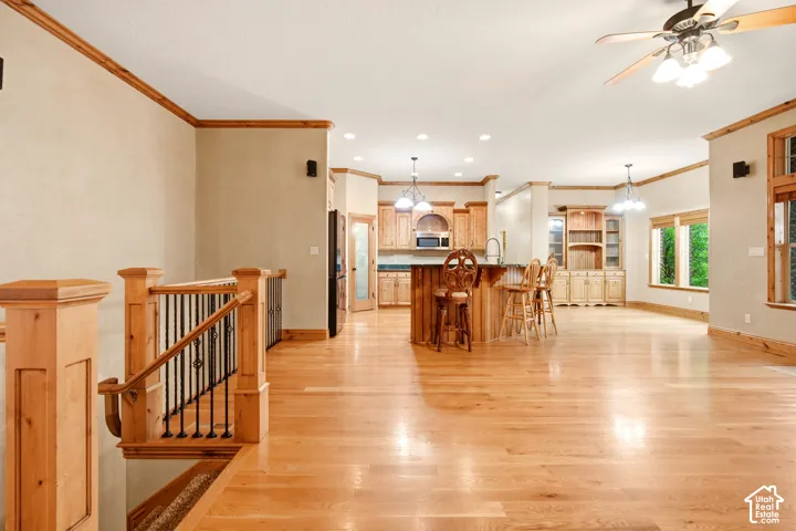 Open-concept interior featuring wood-finish flooring, custom wood cabinetry, a tiered kitchen island with a dark countertop, recessed lighting, and a prominent wood staircase railing with metal balusters