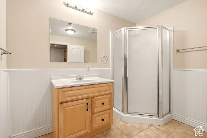 Wood-finish vanity with an integrated basin, white beadboard wainscoting, corner shower stall with a metal frame, tile flooring, and wall-mounted vanity mirror
