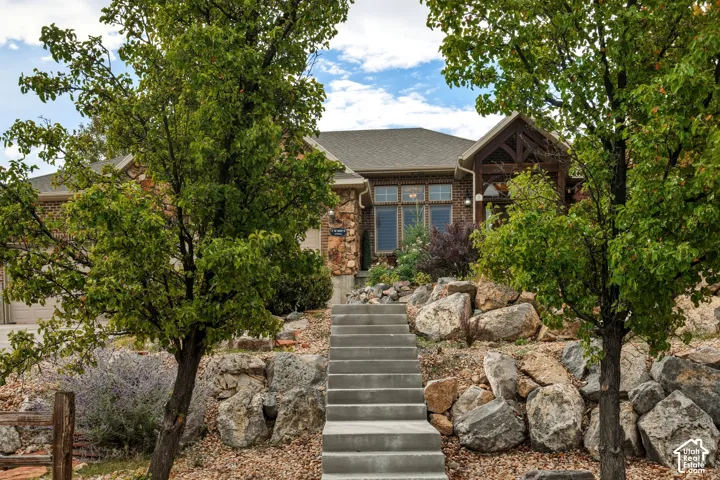 Exterior featuring brick masonry, natural stone accents, timber-frame entryway, concrete staircase, and tiered landscape retaining walls