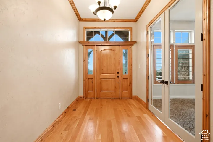 Solid wood entry door with side lights and transom window, wood-finish flooring, crown molding, and double glass-pane doors