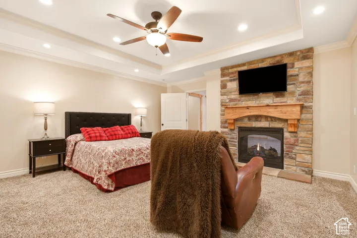 Tray ceiling with recessed lighting, ceiling fan, carpeted flooring, and floor-to-ceiling stone fireplace surround with a natural wood mantel