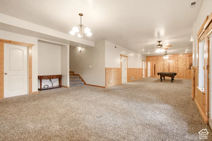 Large interior space featuring wood-panel wainscoting, wall-to-wall carpeting, multiple ceiling fans with light kits, and an overhead chandelier