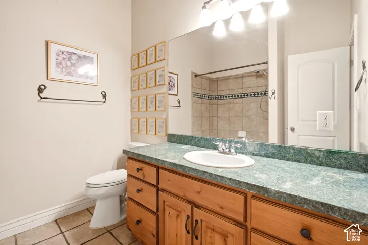 Bathroom featuring a vanity with wood cabinetry, a stone-finish countertop, an integrated oval basin, full-width wall mirror, and tile flooring