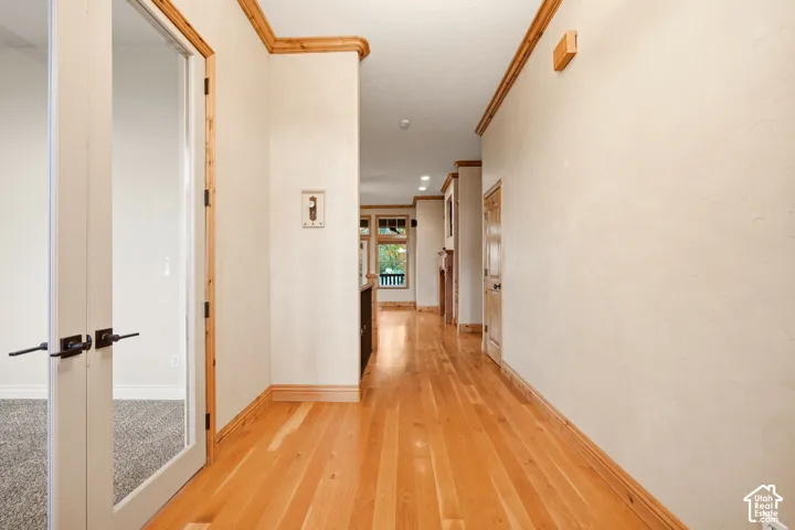 Hallway featuring wood-finish flooring, natural wood crown molding, and glass-paneled double doors with matte black hardware