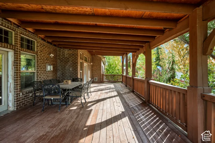 Covered wooden deck featuring exposed beam ceiling, brick exterior wall, and wooden railing