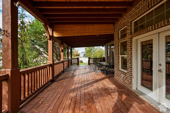 Covered wood deck featuring a natural wood-finish pergola, exposed structural beams, vertical baluster railing, and brick exterior wall